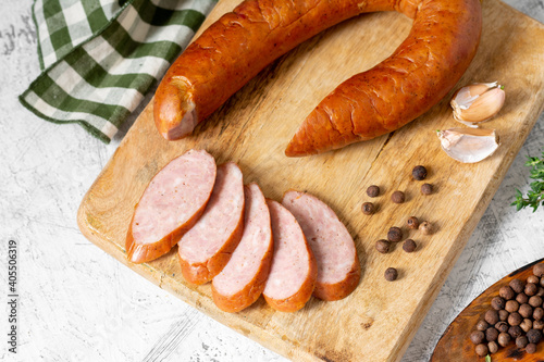 Smoked Cracow sausage on a wooden serving board on a light gray kitchen table. Slicing boiled and smoked sausage 