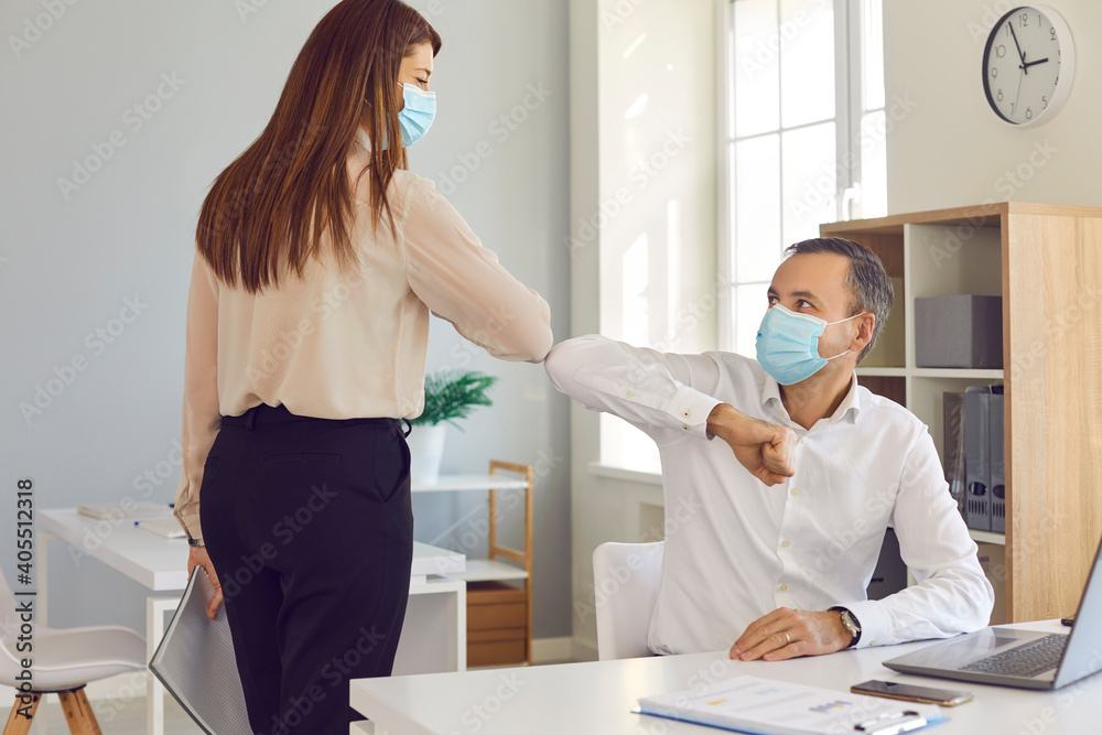 Fototapeta premium Two business people in medical face covering masks greeting each other bumping elbows as a new normal alternative to handshake. Social distancing in office, preventing spread of infection at work
