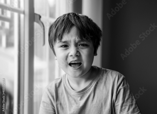 Angry boy siting nex to window,Kid with unhappy face shouting and screaming at camera, Child with crazy or mad yelling, Portrait of emotional little boy with shocked face.Spoild children concept