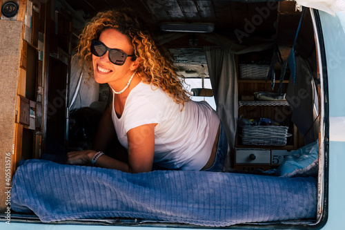 Cheerful and beautiful young adult woman smile lay down inside a trendy van vehicle during travel and summer holiday vacation lifestyle - portrait of pretty blonde long hair people enjoy the life photo