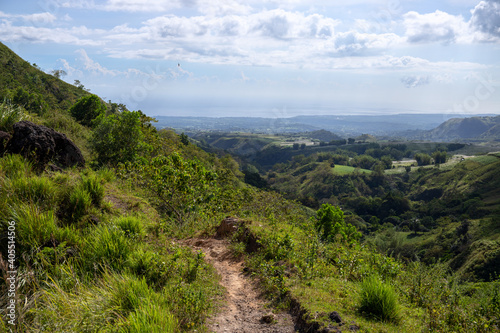 Tropical island landscape with green hills and hiking path. Green summer nature scenic view. South Asia travelling. Hiking tour in the Philippines. Untouched environment of tropical island