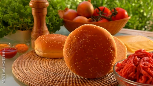 Cesam bun is rolling on the table on the background of the ingredients for cheeseburger preparation photo