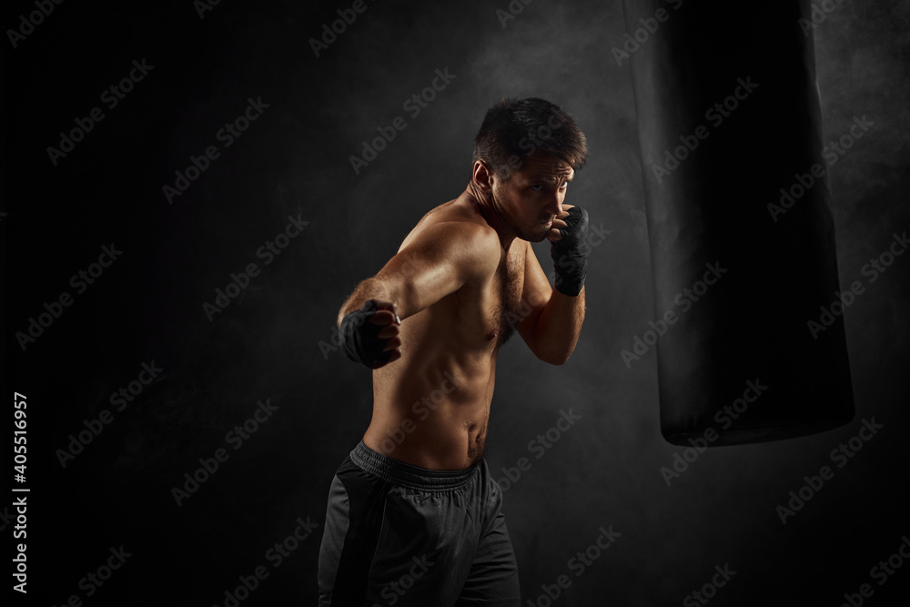 Male boxer training defense and attacks in boxing bag on black background