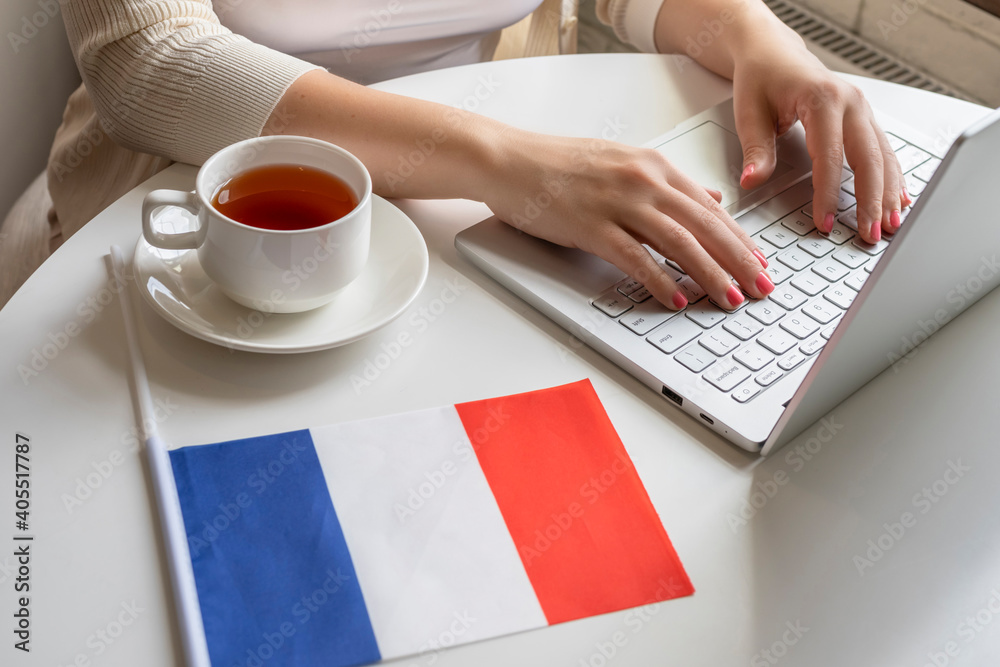 Lonely woman freelancer with flag of France, enjoying having breakfast with cup of coffee working on laptop sitting near window in cafe at morning.