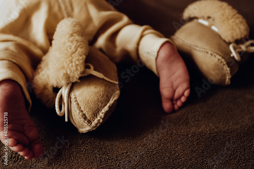 Toes of newborn baby with warm sheepskin booties and thermo pants in beige warm colors