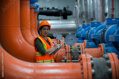 Blur Young female mechanical engineer holding drawing to checking and inspection of HVAC heating ventilation air conditioning system and pipping line of industrial construction at  plant.