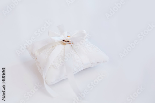 Two golden engagement wedding rings at white small decor pillow cushion with ribbon 