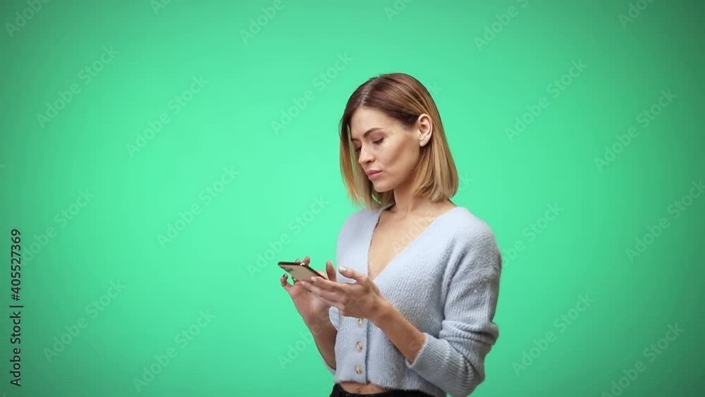 happy beautiful blonde caucasian woman in casual clothes using mobile cell phone and typing sms message on green color background in studio. happy beautiful blonde caucasian woman in casual clothes using mobile cell phone and typing sms message on green color background in studio.