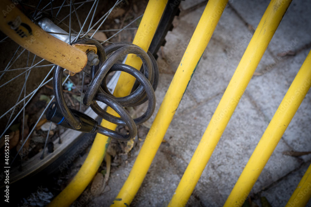 Black bicycle safety locker and wheel on a yellow pole of a bike parking