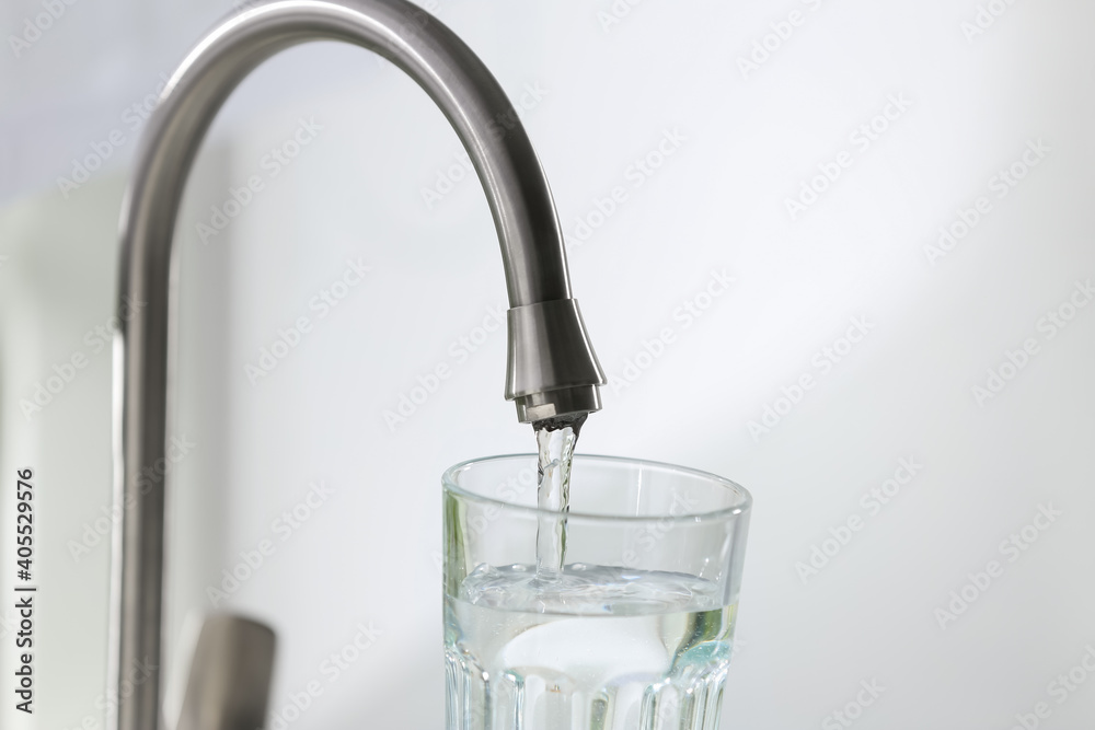 Filling glass with clear water from faucet on light background, closeup Filling glass with clear water from faucet on light background, closeup