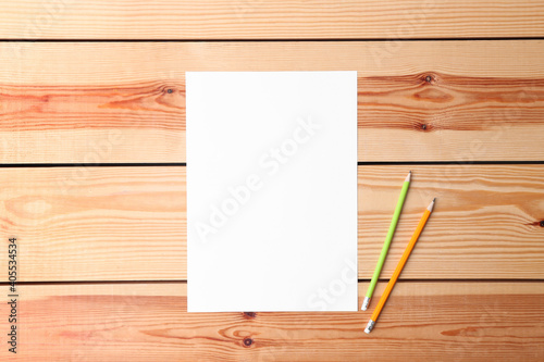 Blank paper sheet and pencils on wooden background, flat lay. Space for text