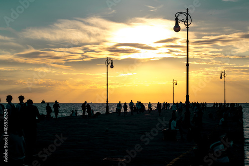 Tramonto invernale giallo, persone che camminano su un molo controluce