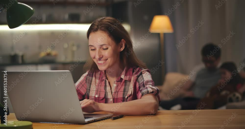 Businesswoman working from home on laptop with husband and daughter relaxing on couch Businesswoman working from home on laptop with husband and daughter relaxing on couch
