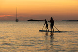 Two people on the same board of paddle surf at sunset