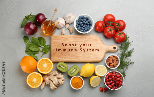 Set of natural products and wooden board with text Boost Your Immune System on grey table, flat lay photo