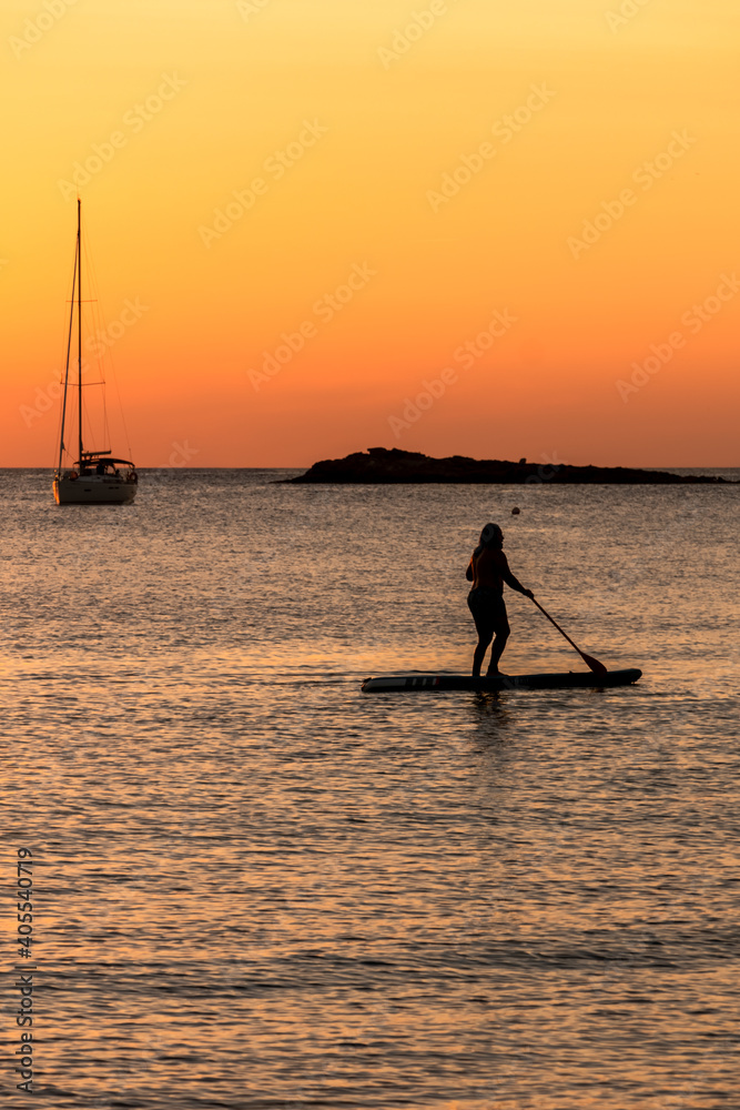 Silhouette of man on stand up paddle board at sunset and a sailboat