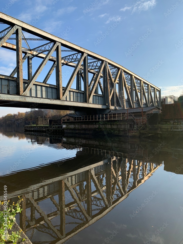 Old metal bridge going over the Manchester ship canal with reflections in the water and a blue sky background. Old metal bridge going over the Manchester ship canal with reflections in the water and a blue sky background.