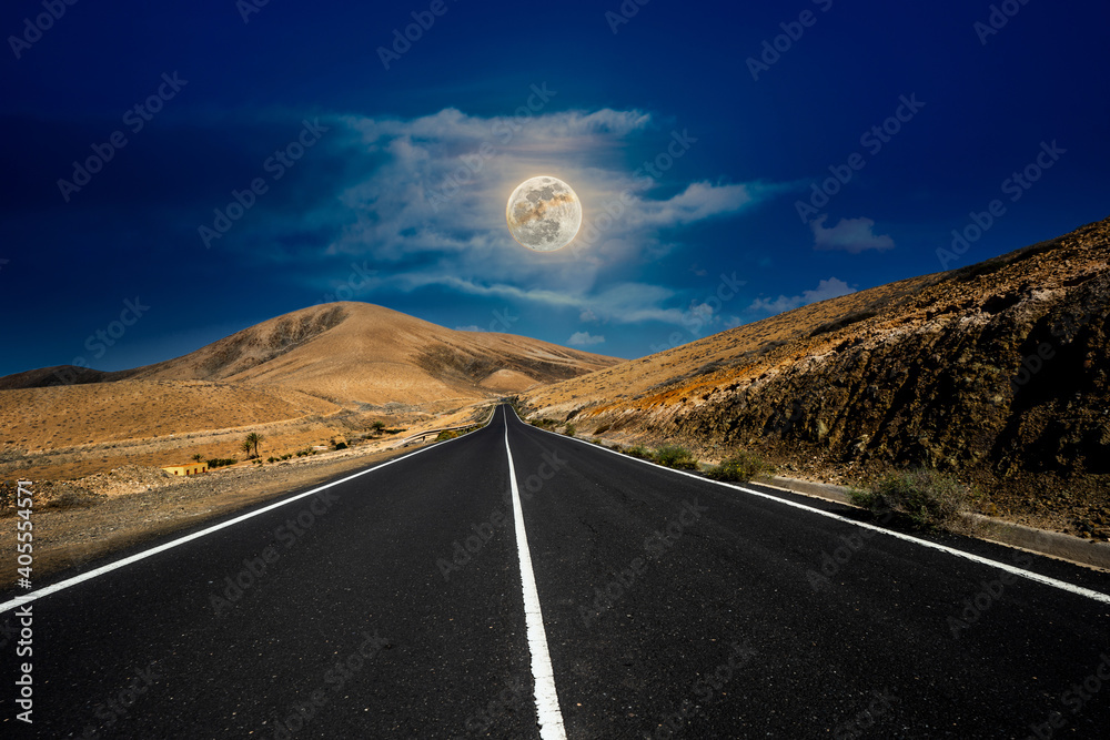 Asphalt road in the mountains with the moon in the sky