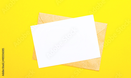 On a yellow-colored background, an envelope and a blank card with space to insert text or illustrations. Top view with copy space