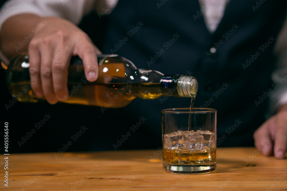 Barman pouring whiskey wearing protective mask on the bar counter