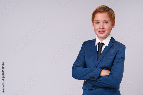 Cheerful school kid with red hair in formal clothes with his arms crossed isolated over grey background