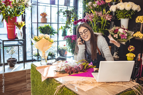 Women florist looking laptop got order at counter of her flower shop, occupation working concept. Smiling flower shop owner working on laptop computer. Woman standing at counter.