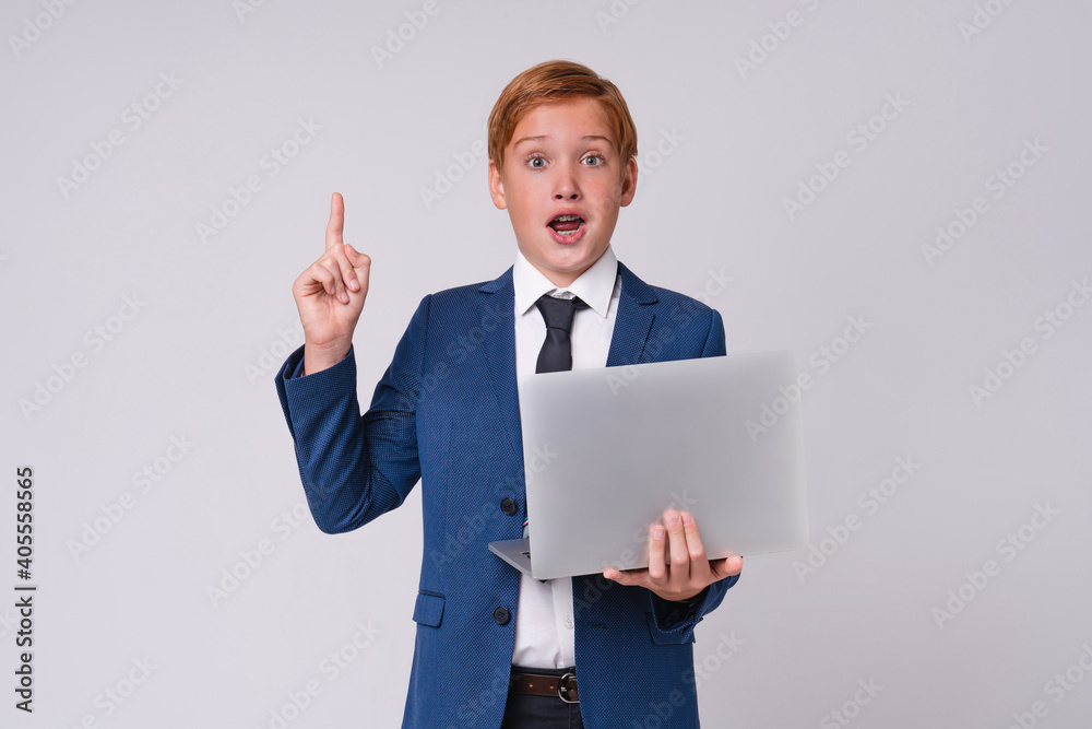 Red-haired smart preteen boy with braces having an idea with laptop isolated over grey background Red-haired smart preteen boy with braces having an idea with laptop isolated over grey background