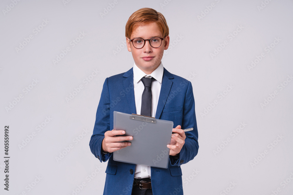 Cropped portrait of redhead preteen boy in formal clothes using clipboard isolated over grey background Cropped portrait of redhead preteen boy in formal clothes using clipboard isolated over grey background