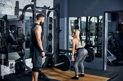 Trainer watching a female lifting a barbell