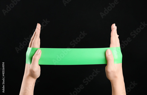 Woman with fitness elastic band on black background, closeup