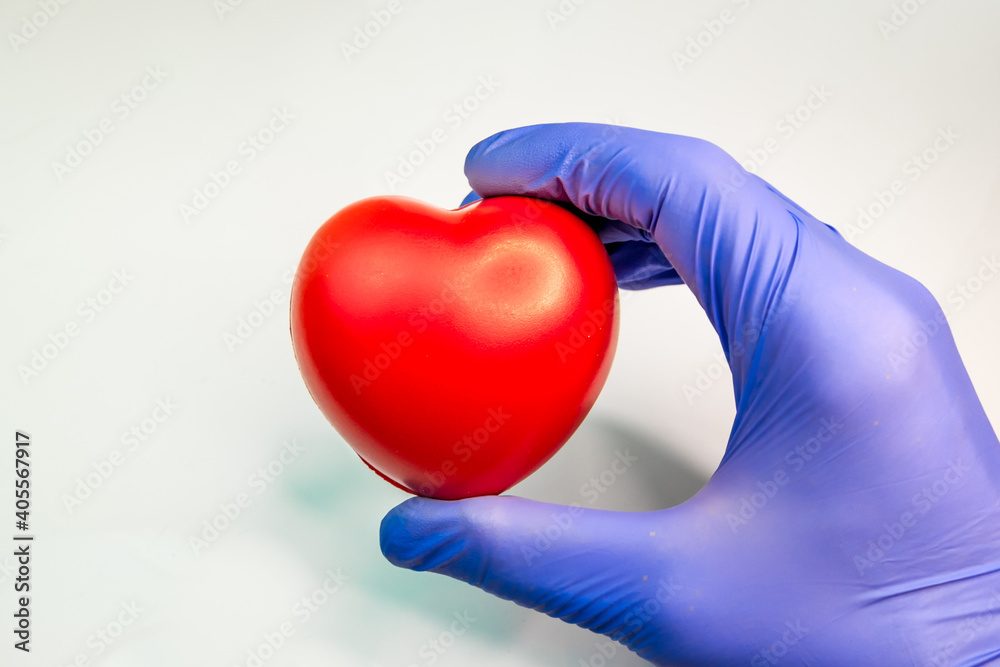 male hand in medical gloves holding a toy red heart male hand in medical gloves holding a toy red heart