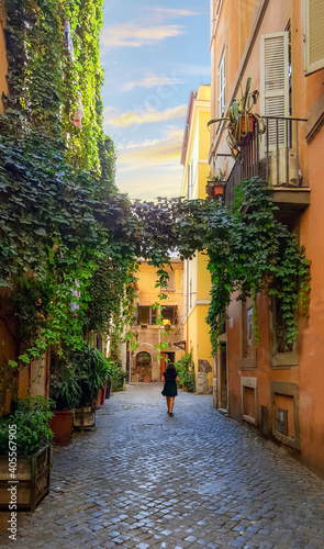 Fototapeta Naklejka Na Ścianę i Meble -  A solo female walks through an ivy covered colorful alley in the Trastevere district of Rome, Italy