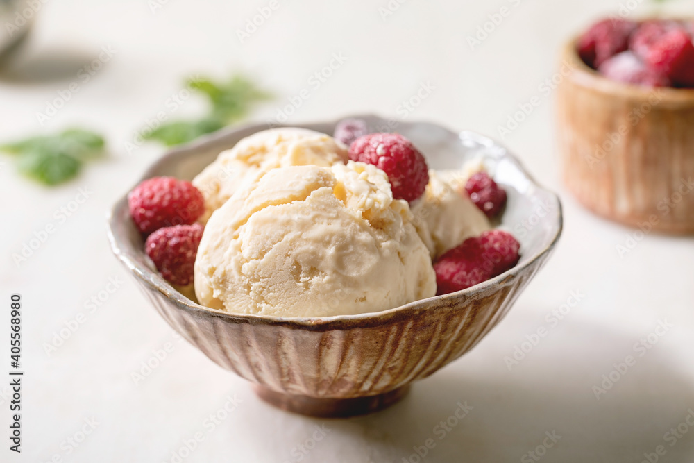 Homemade caramel vanilla ice cream with frozen raspberries in ceramic bowl standing on white marble table with flowers behind. Homemade caramel vanilla ice cream with frozen raspberries in ceramic bowl standing on white marble table with flowers behind.