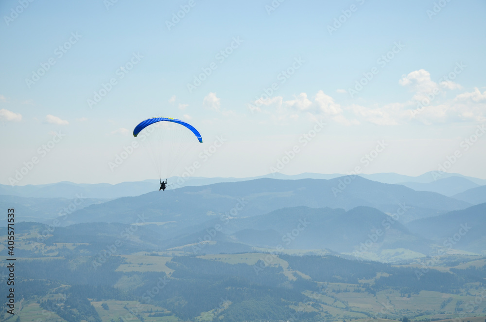 Paraglider flies in the sky over the mountains on a bright sunny day. Paragliding in the sky. Extreme sport.
