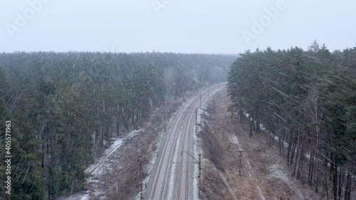 Drone flying over a railroad in heavy snowfall. Railway in winter forest from aerial view. photo