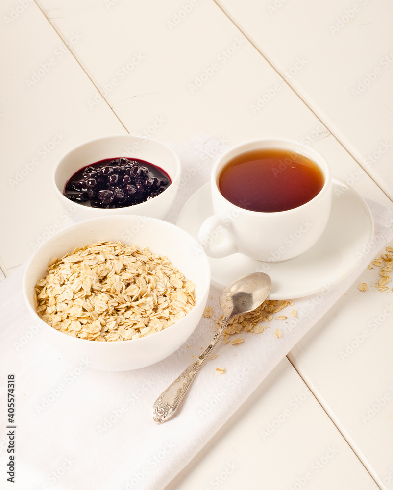 white cup of tea and a plate of oatmeal with currant jam on white background white cup of tea and a plate of oatmeal with currant jam on white background