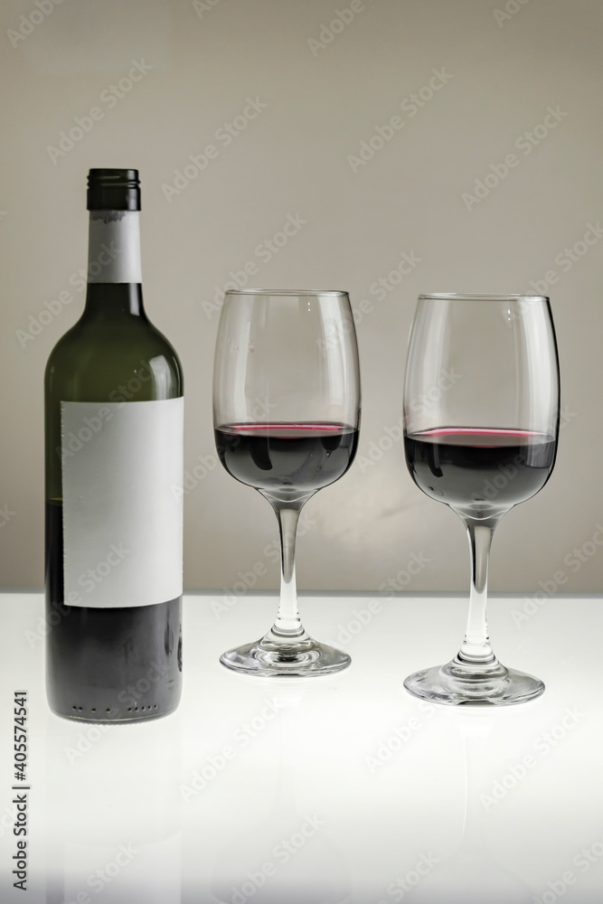 Vertical shot. Two large glasses with red wine and a bottle on a blurred background, close-up.
