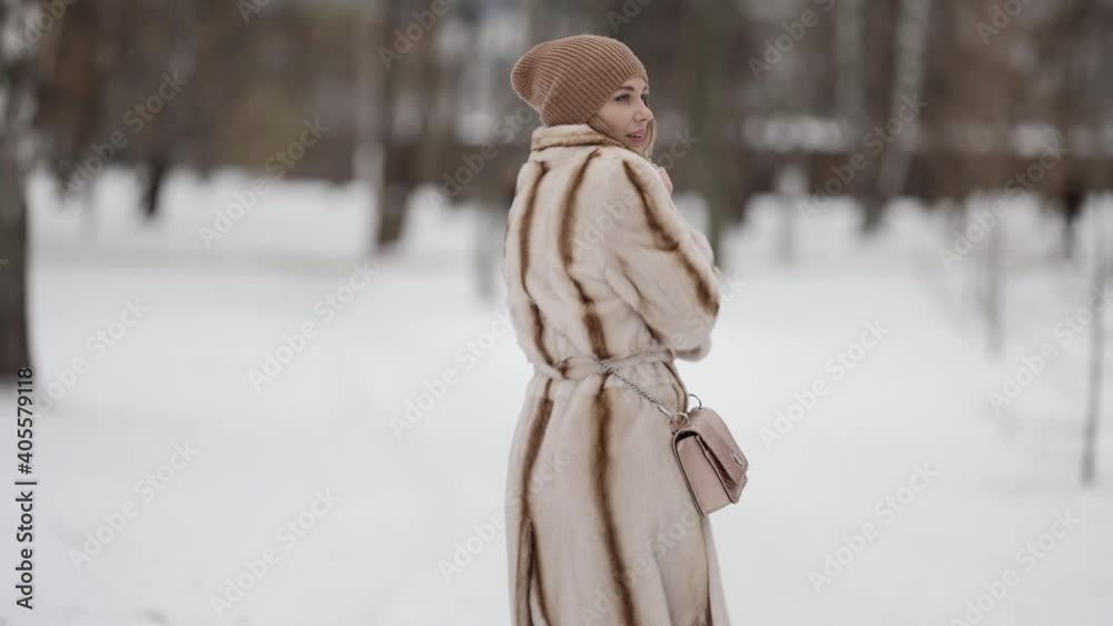 An attractive fashionable blonde in a beautiful fur coat and a beige hat poses against the background of a winter park. Model on a snowy background of winter weather. An attractive fashionable blonde in a beautiful fur coat and a beige hat poses against the background of a winter park. Model on a snowy background of winter weather.