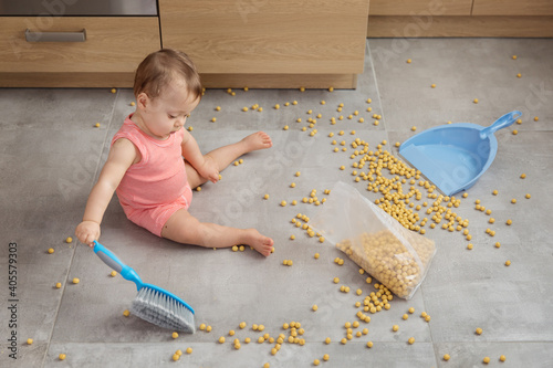 Cute baby sweeping up spilled cereal on kitchen floor photo