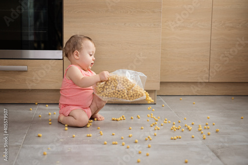 Cute baby spilling cereal on kitchen floor