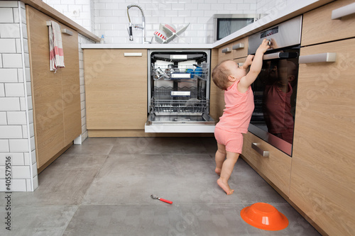 Cute toddler in kitchen touching oven knob