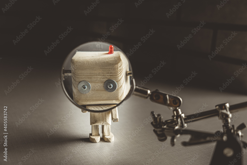 Fototapeta premium wooden robot android stands on a table under a magnifying glass. metal clamps with a magnifying glass. the face of a robot in the beautifying glass. human study concept