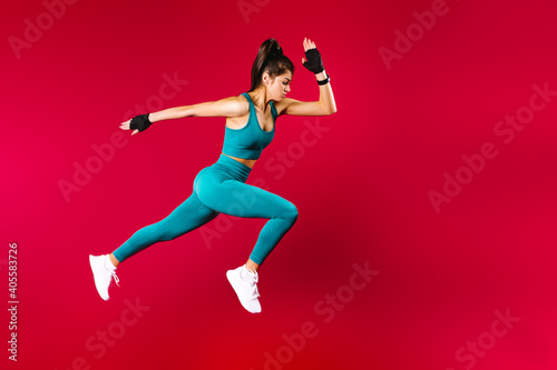 Sporty woman runner in silhouette on red background. Photo of attractive woman in fashionable sportswear. Dynamic movement. Side view. Sport and healthy lifestyle