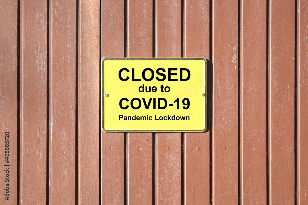 Shuttered wooden gate with a yellow sign and text Closed due to Covid-19 Pandemic Lockdown, many retailers are forced to do this during the coronavirus crisis, copy space Shuttered wooden gate with a yellow sign and text Closed due to Covid-19 Pandemic Lockdown, many retailers are forced to do this during the coronavirus crisis, copy space