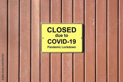 Shuttered wooden gate with a yellow sign and text Closed due to Covid-19 Pandemic Lockdown, many retailers are forced to do this during the coronavirus crisis, copy space