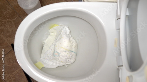 Close-up tossing a dirty baby diaper into the toilet. It clogs the toilet flush