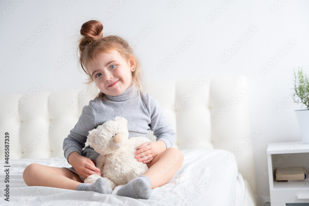 little girl in grey turtleneck playing with teddy bear on white bedding little girl in grey turtleneck playing with teddy bear on white bedding