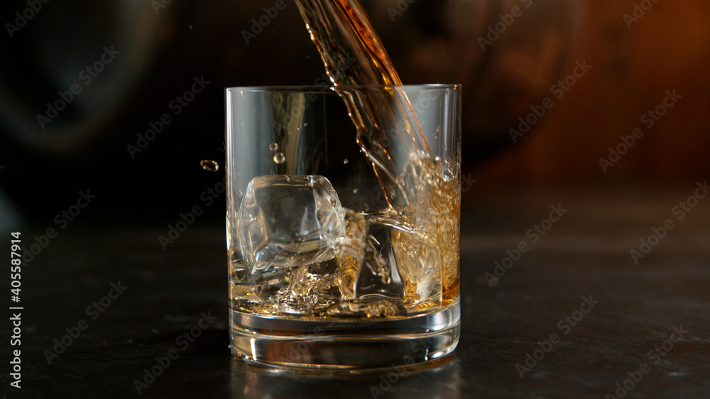 Glass of whisky with splashing liquid and ice rocks inside.