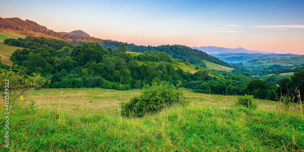 mountainous rural landscape at dawn. beautiful scenery with forests, hills and meadows in morning light. ridge with high peak in the distance. village in the distant valley