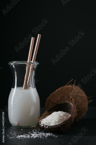 Bottle of coconut vegan milk with straws, whole coconut and flakes on black background. Healthy lifestyle concept.